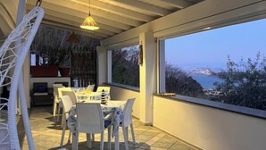 Un comedor con una mesa dispuesta para cuatro personas, un sillón colgante y vista al mar.