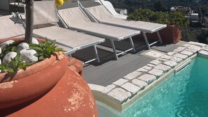 Zona de piscina con sillones de descanso, un limonero en maceta y vistas al mar y a las montañas.