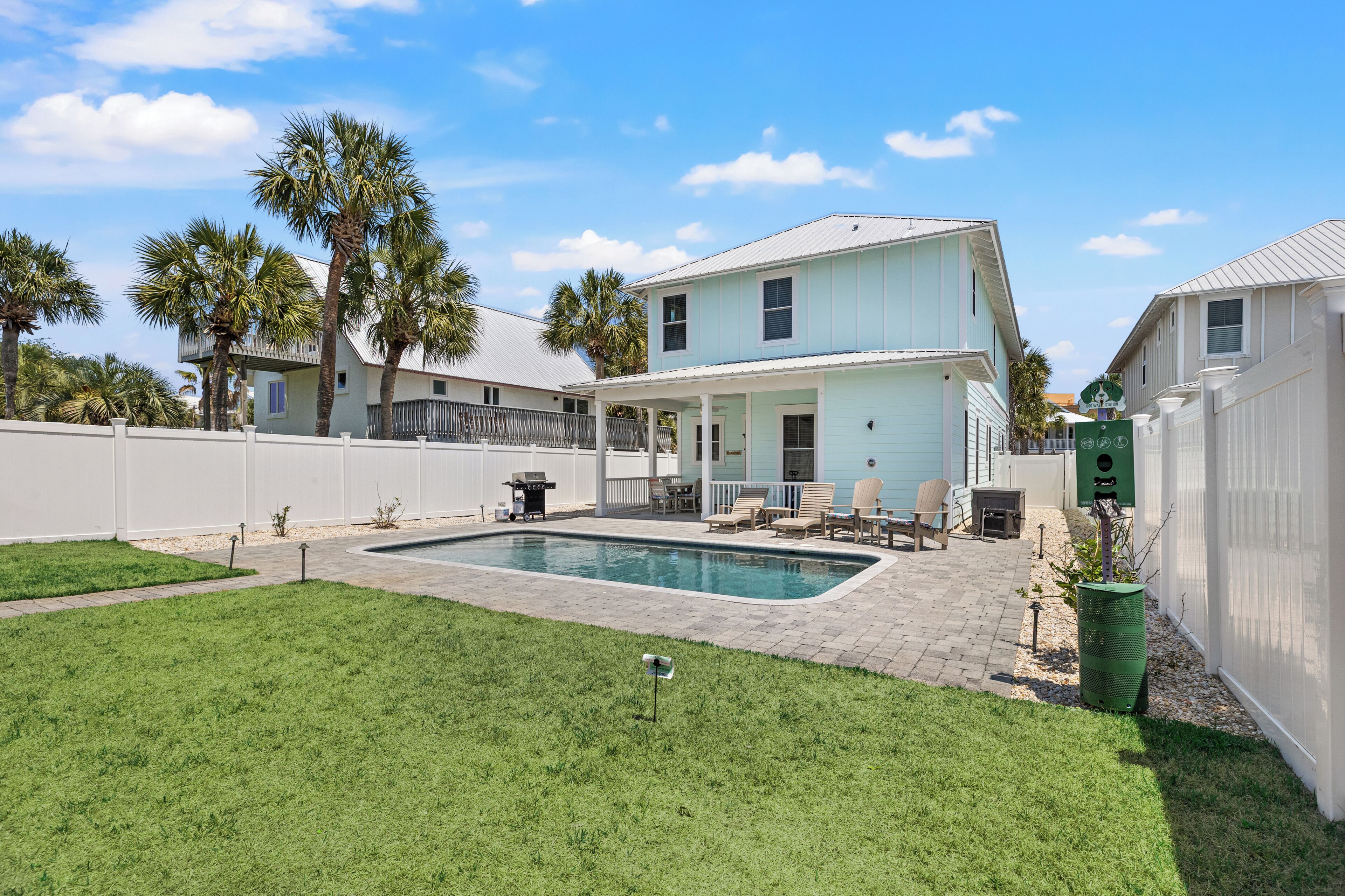 Una casa de dos pisos con piscina, patio trasero cercado y palmeras.