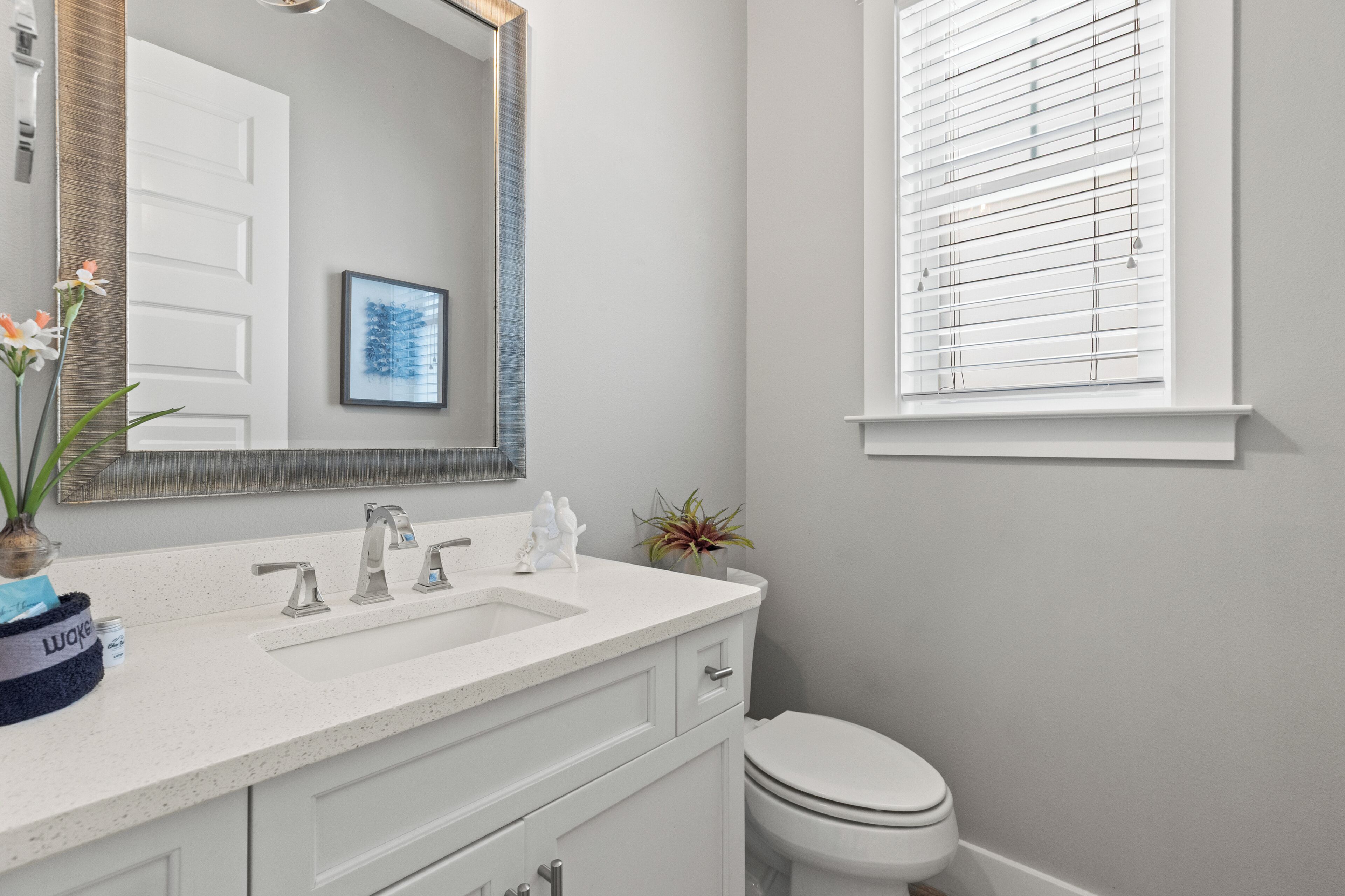 A bathroom with a white sink, a mirror, a toilet, and a window with blinds.