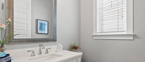 A bathroom with a white sink, a mirror, a toilet, and a window with blinds.