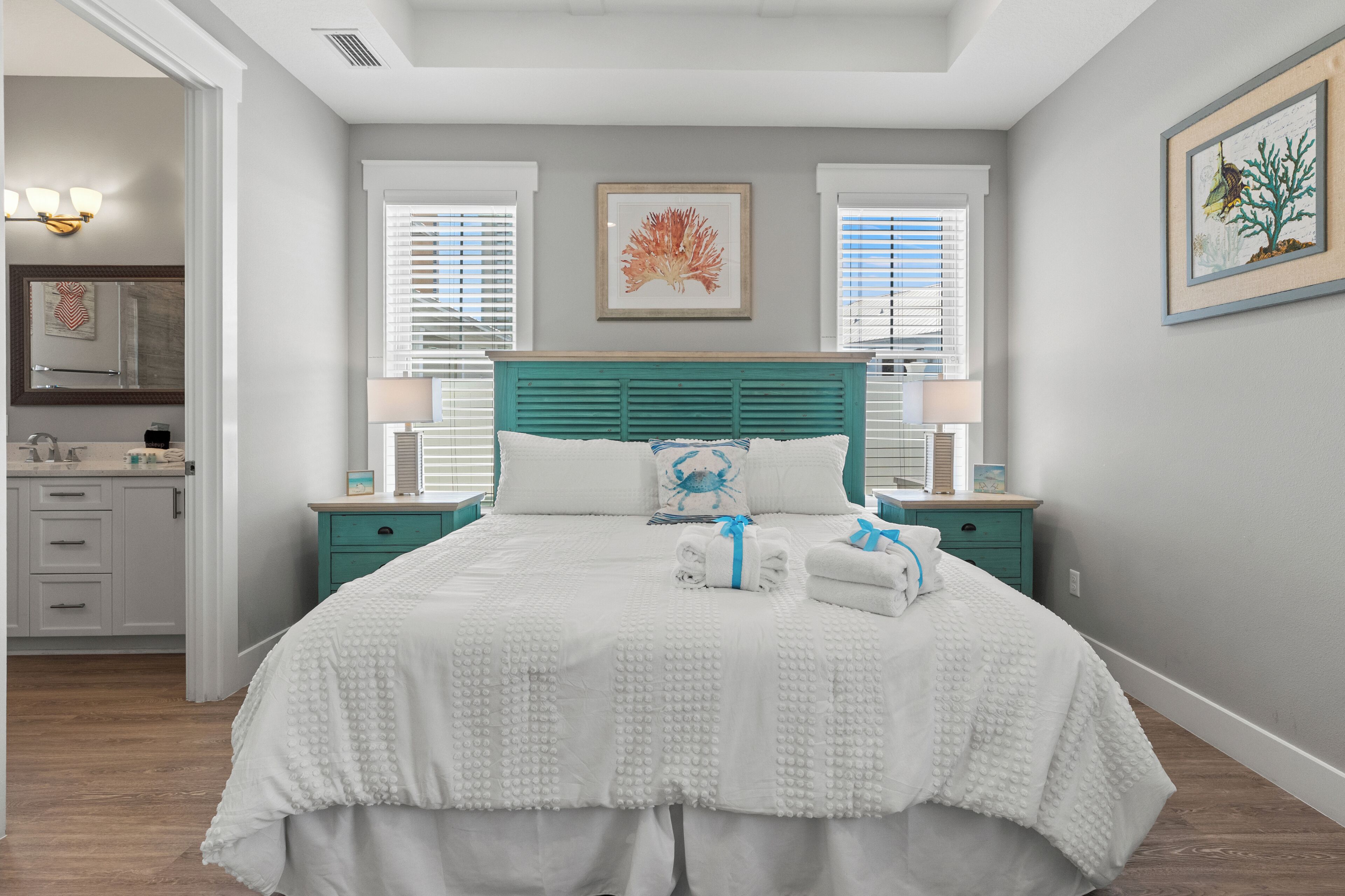 A bedroom with a bed, two bedside tables, a nightstand, a window, and a door leading to a bathroom.
