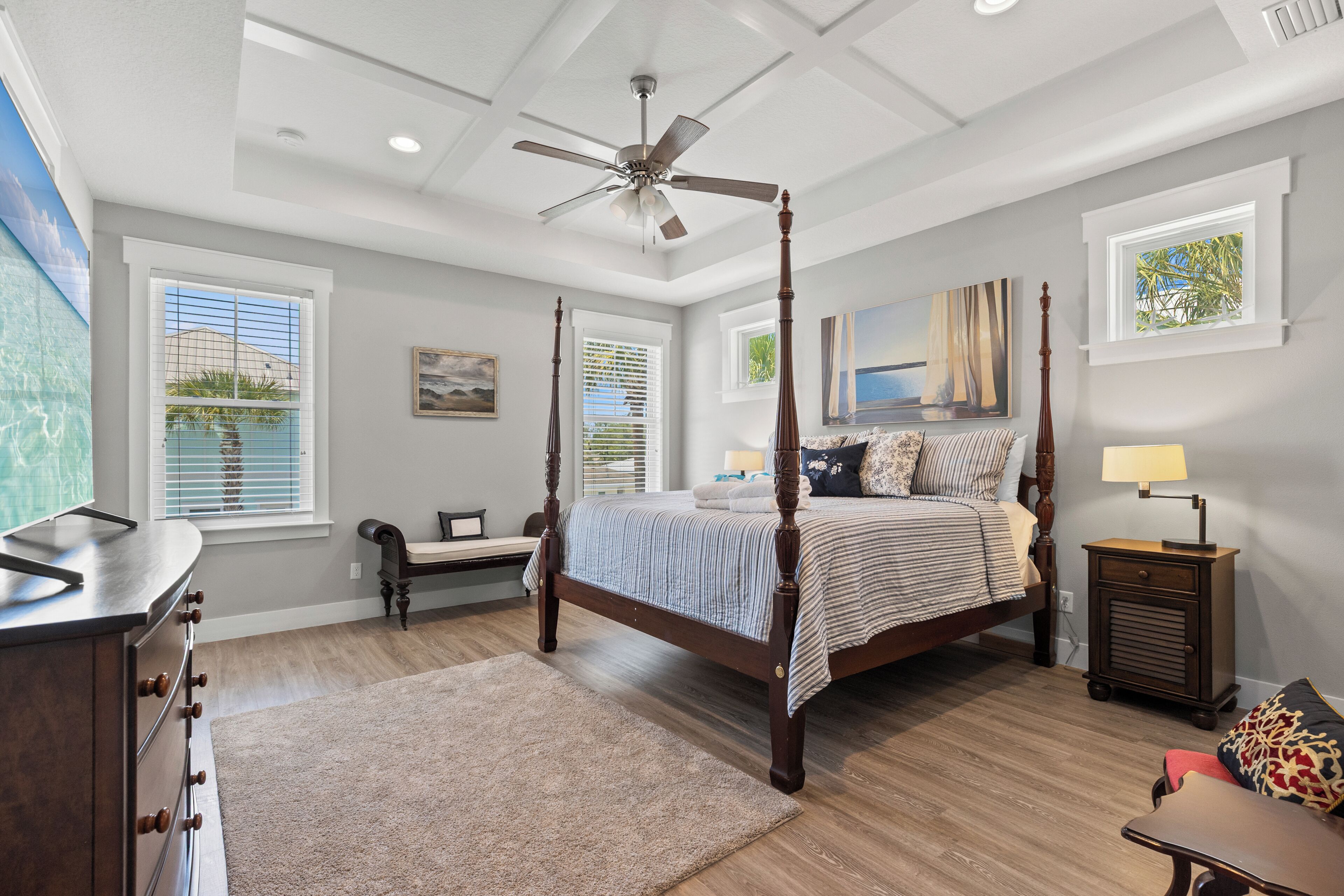 A bedroom with a four-poster bed, a ceiling fan, a nightstand, a lamp, and a view of the outdoors through the window.