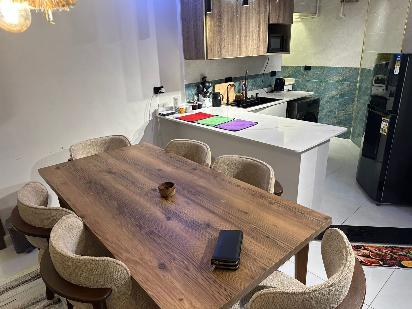 Comedor con mesa de madera y seis sillas, cocina al fondo y una pequeña isla con microondas y lavaplatos.