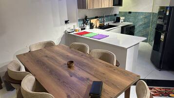Comedor con mesa de madera y seis sillas, cocina al fondo y una pequeña isla con microondas y lavaplatos.