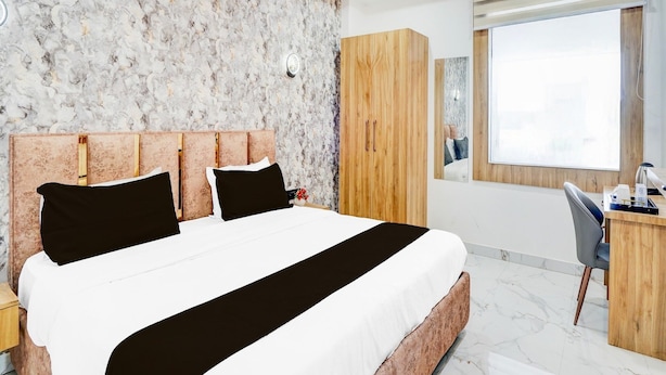 Ein modernes Hotelzimmer mit Wand im Marmoroptik, einem großen Bett mit Holz-Kopfschild, einem Schreibtisch mit Stuhl und einem großen Fenster.