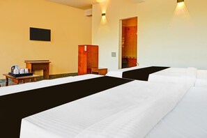A hotel room with two beds, a desk, a chair, a television, and a door leading to a bathroom. - Deluxe Hotel Raj (Madikeri)