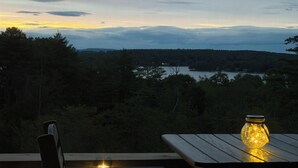 A wooden table and chair set outdoors with a view of a lake and forested hills in the background. - Walk to Weirs Beach Boardwalk with Treetop Views of Lake Winnipesaukee! (Laconia)