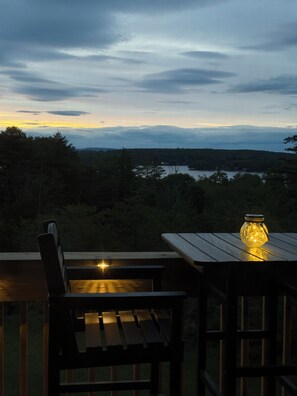 A wooden table and chair set outdoors with a view of a lake and forested hills in the background. - Walk to Weirs Beach Boardwalk with Treetop Views of Lake Winnipesaukee! (Laconia)