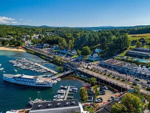 A marina with boats docked, a pier, and buildings with visible windows and storefronts. - Walk to Weirs Beach Boardwalk with Treetop Views of Lake Winnipesaukee! (Laconia)