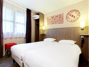 A hotel room with two beds, a red bench, a window with curtains, and a wall with a U.S.A. stamp and text. - Kyriad Cholet (Cholet)