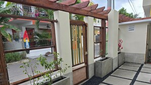 Un espace extérieur abrité, doté de jardinières en béton, d’une pergola en bois et d’un chemin recouvert de carreaux.