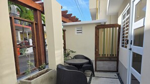 Une petite terrasse extérieure avec une table et des chaises, une porte en bois et une vue sur la rue.