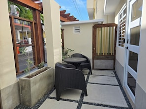 A small outdoor patio with a table and chairs, a wooden gate, and a view of the street.