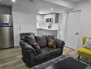 A modern living room with a grey sofa, a black coffee table, a yellow armchair, and a kitchen in the background. - Cozy Winnipeg Retreat  (Winnipeg)