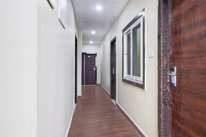 A hallway with a wooden floor, white walls, and a door at the end. - Deluxehotel Rans (Hyderabad)