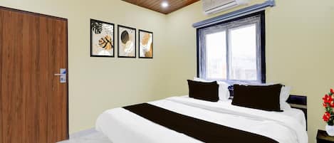 A hotel room with a bed, a window, a door, and three framed artworks on the wall.