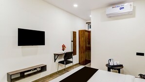 A modern hotel room with a bed, a desk with a chair, a TV mounted on the wall, a wardrobe, and a small table with toiletries. - Deluxe Tolkanti Arc (Hyderabad)