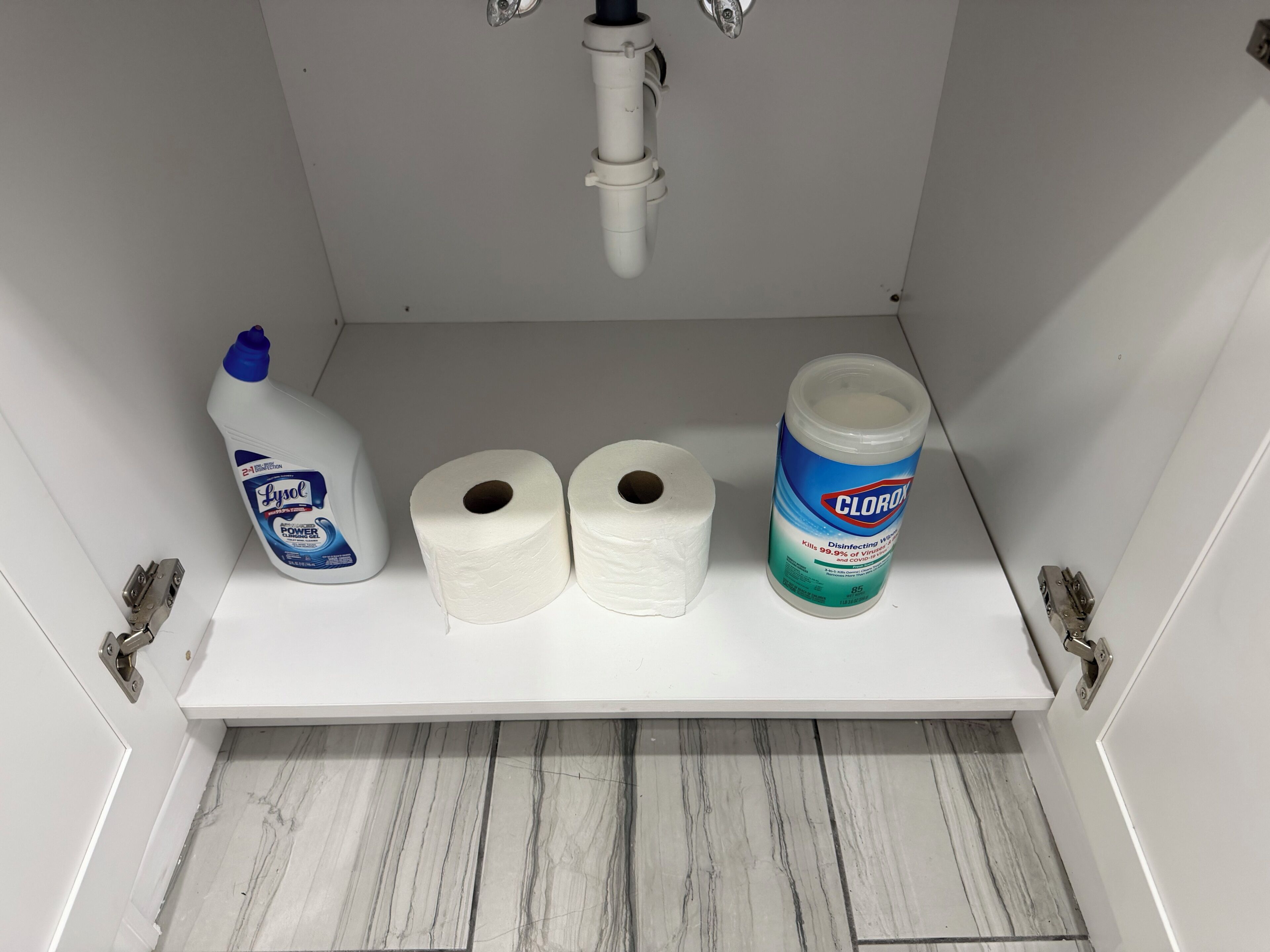 Een badkamerschaar met Lysol ontsmettingsdoekjes, twee toiletrollen en een fles Clorox ontsmettingsmiddel.