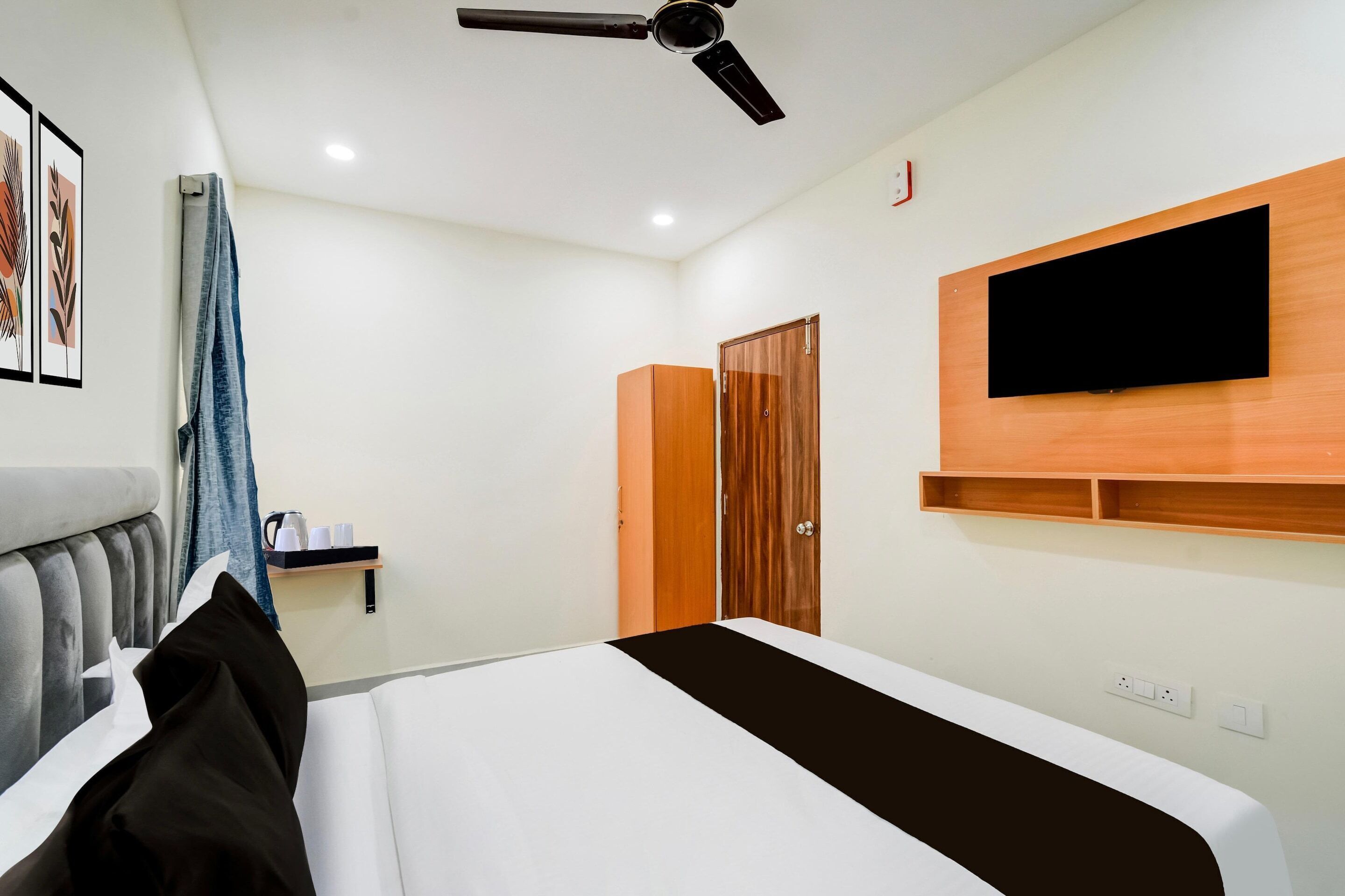 Una habitación de hotel con una cama, ventilador de techo, televisor montado en la pared y armario de madera.
