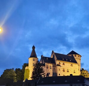 A large stone castle with multiple towers and a prominent central tower, surrounded by trees and under a clear sky.