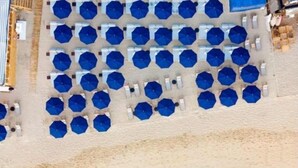 Ein Strand mit Reihen aus blauen Sonnenschirmen und weißen Liegestühlen.