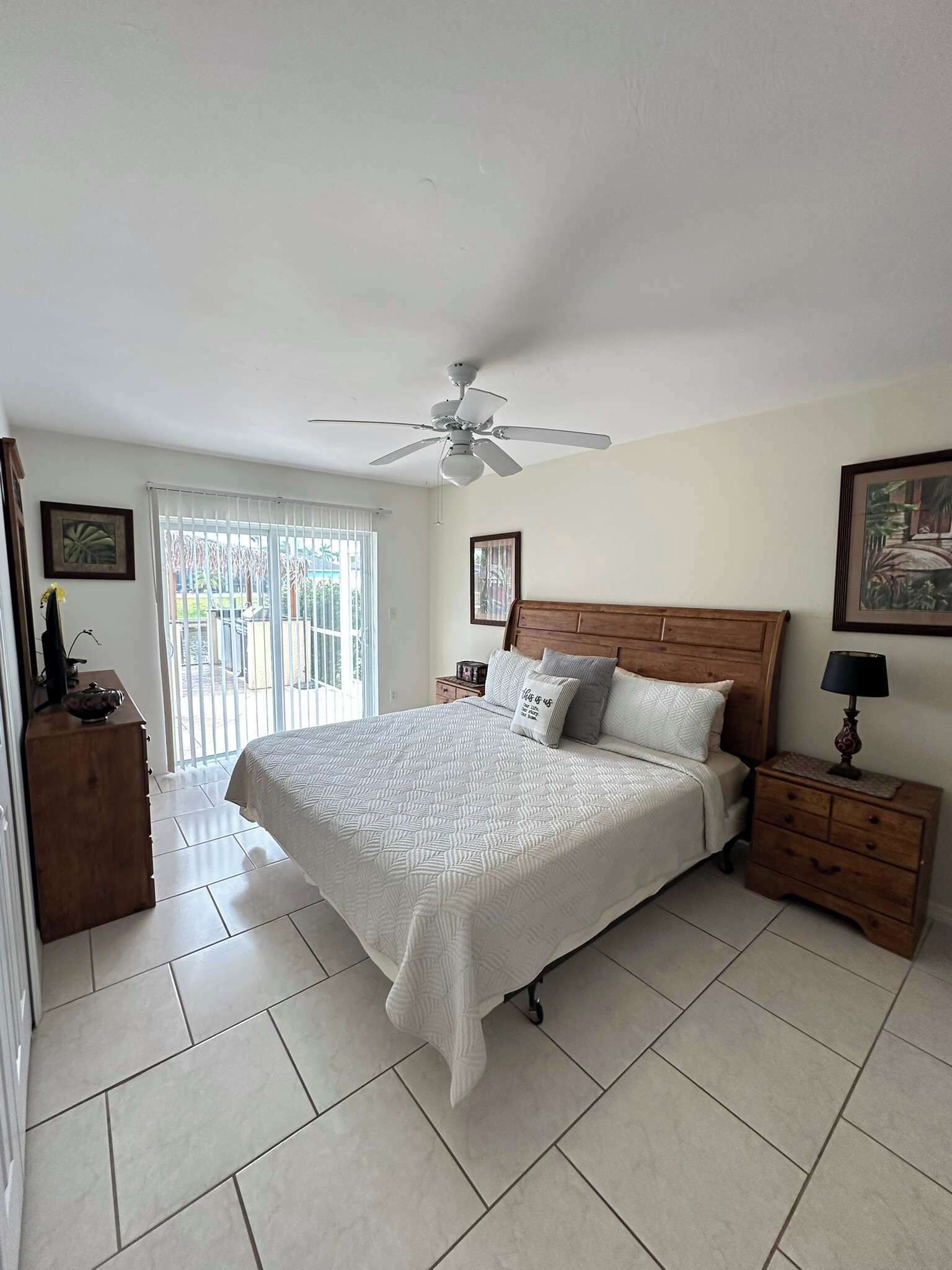 A bedroom with a bed, a ceiling fan, a nightstand, a dresser, and a window with blinds.