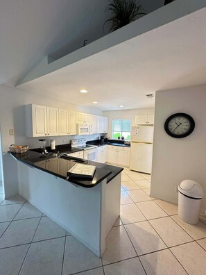 A modern kitchen with white cabinets, a black countertop, and a built-in island. - Villa Blue Water - Cape Coral (Cape Coral)