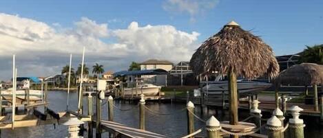 A marina with boats docked, wooden piers, and thatched-roof structures.
