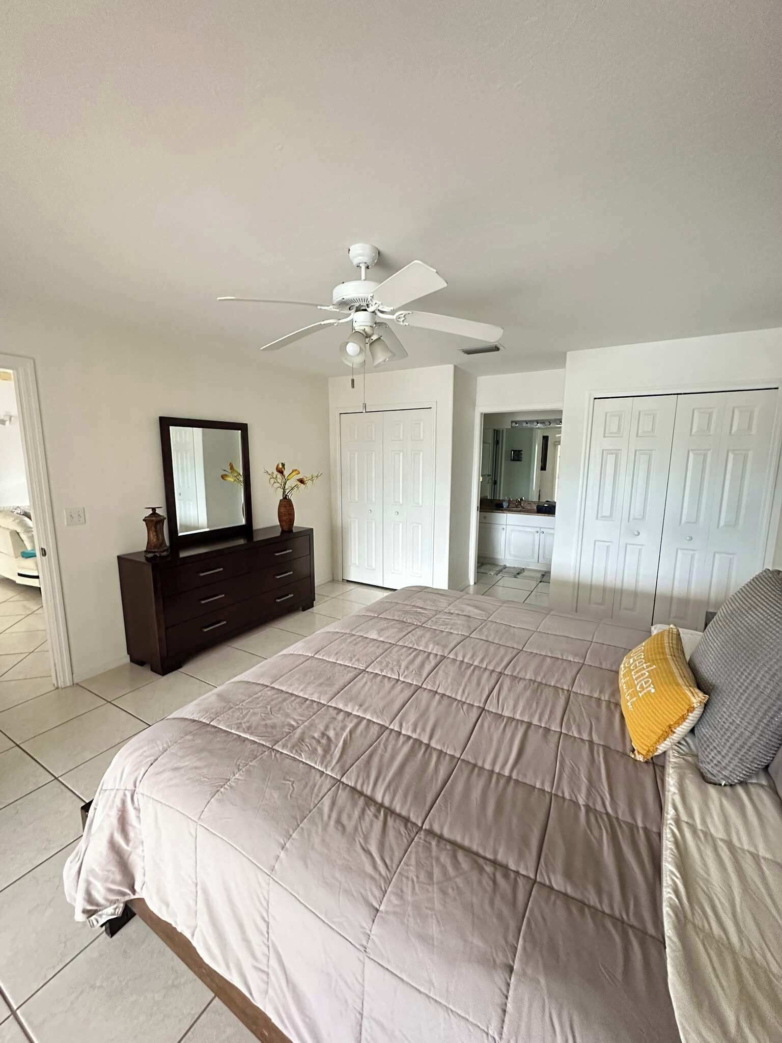 Une chambre à coucher avec un lit, une commode, un ventilateur de plafond et des portes blanches.