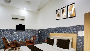Ein Hotelzimmer mit einem Bett, zwei Sesseln, einem kleinen Tisch, einem Fernseher und drei gerahmten Bildern an der Wand.