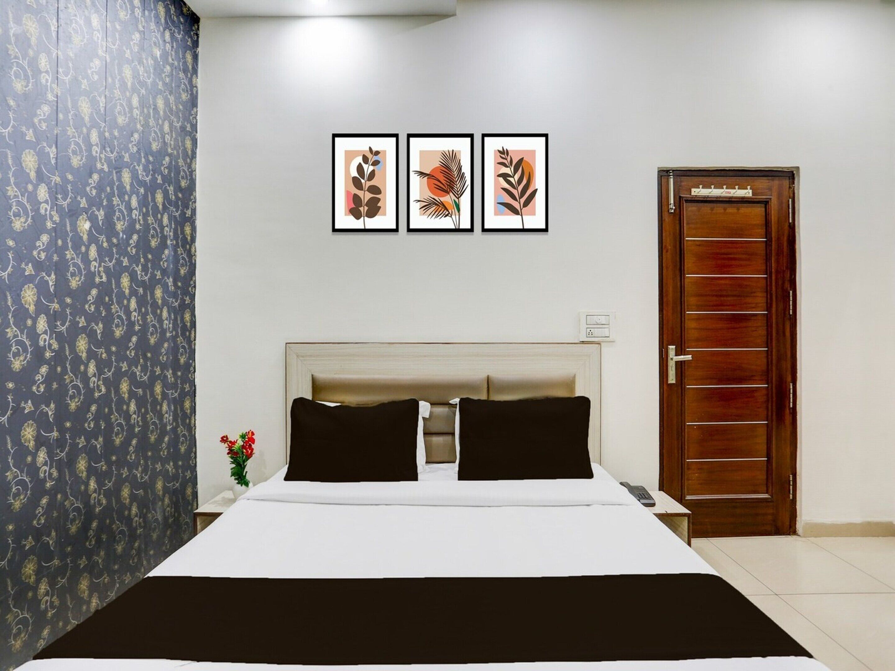 Una camera d'albergo con un letto, un comodino, una porta in legno e tre quadri appesi al muro.