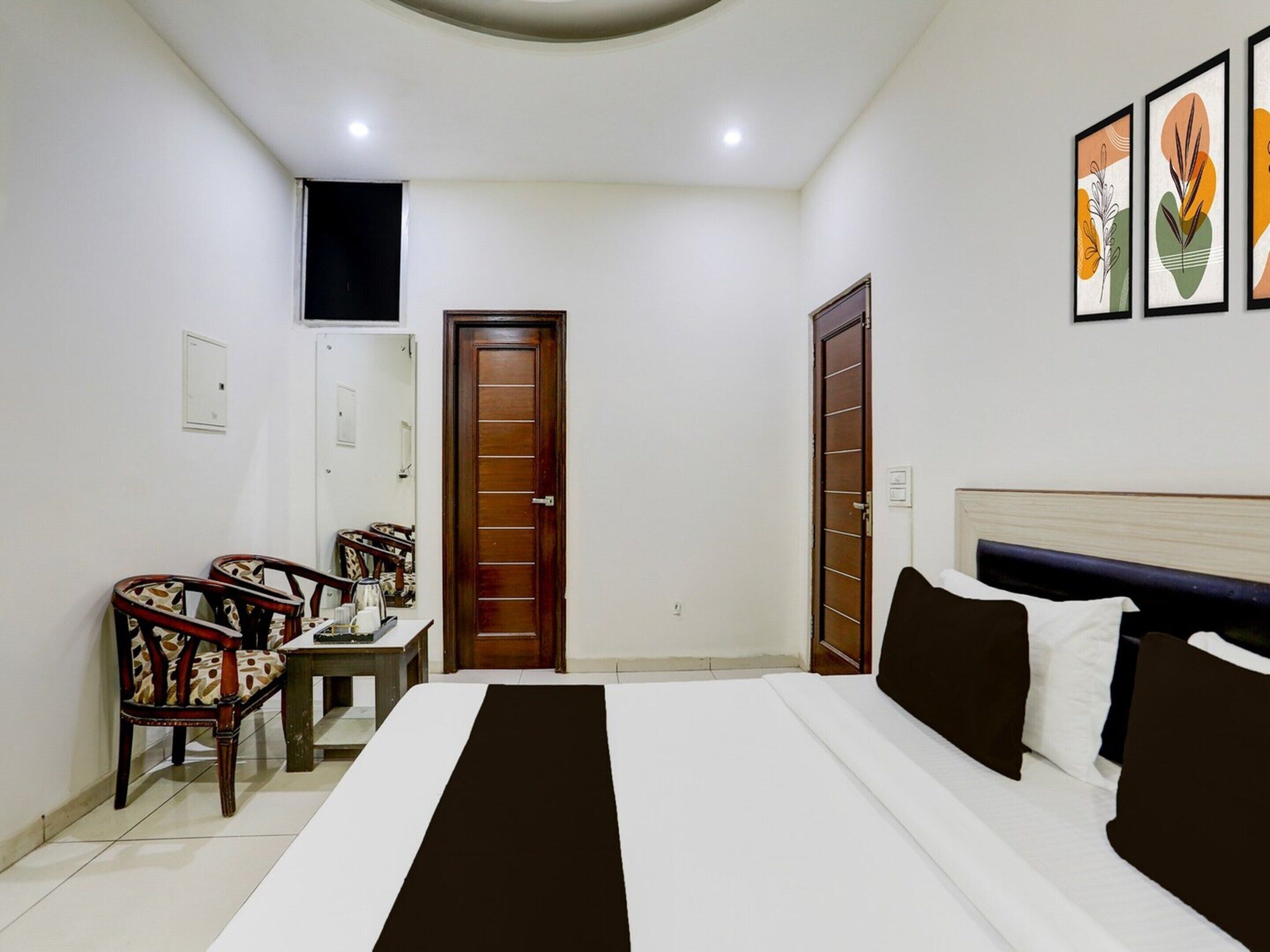 A bedroom with a bed, two doors, a small table with chairs, and framed artwork on the wall.