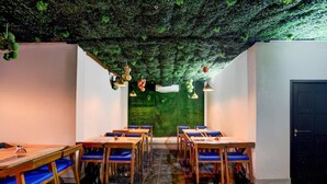 Un restaurante con pared y techo verdes, mesas de madera con sillas azules y adornos colgantes.