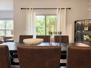 A dining area with a table, chairs, a bowl, candles, and a window with curtains.