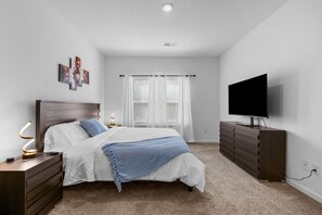 A bedroom with a bed, a dresser, a TV, and a window with blinds.