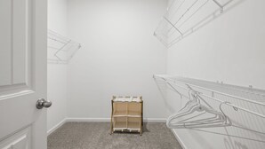 A room with white walls, a door, a small wooden shelf, and metal wire shelves.