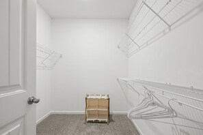 Una habitación con paredes blancas, una puerta, un estante de madera pequeño y repisas de alambre metálico.