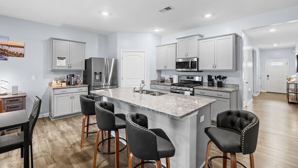 A modern kitchen with a central island, bar stools, stainless steel appliances, and light gray cabinetry.