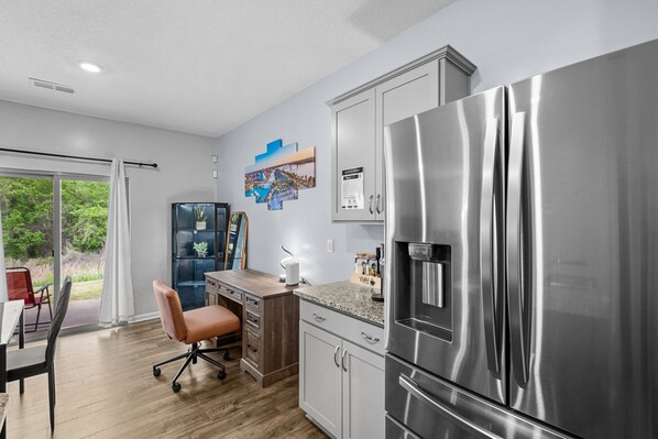 A modern kitchen with stainless steel appliances, a wooden dining table, and a view of greenery outside.
