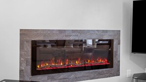 A modern fireplace with a glass front, a flat-screen TV mounted on the wall, and a stone-textured surround.