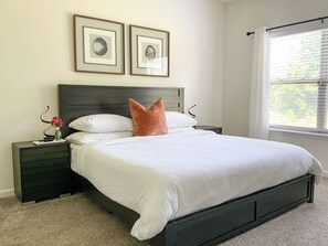 A bedroom with a bed, nightstands, a window with blinds, and framed pictures on the wall.