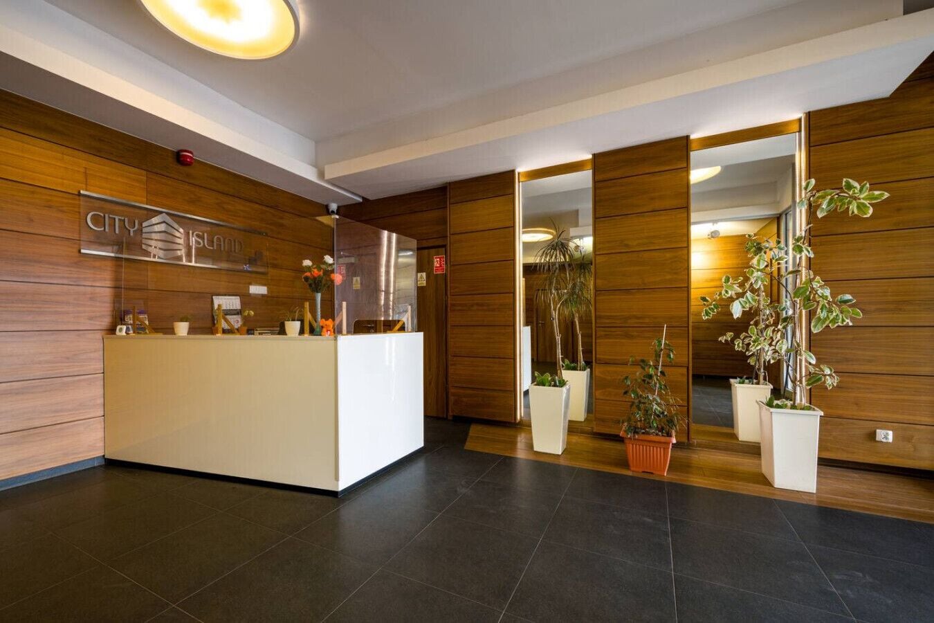 Un área de recepción con un mostrador de madera, un letrero 'CITY' y plantas en macetas.