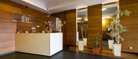 Un área de recepción con un mostrador de madera, un letrero 'CITY' y plantas en macetas.