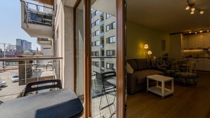 Een balkon met een tafel en stoelen, een woonkamer met een bank en een kleintje tafeltje, en een keukenhoek.