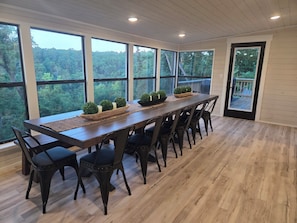 Un comedor con una mesa larga, sillas y grandes ventanales con vistas al bosque.