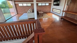 A spacious room with a wooden floor, a white sofa, a small table, and a TV mounted on the wall. - Rustic and cozy beach house with 4 ensuites (Vila Velha)