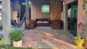 A covered patio with a brick floor, a wicker sofa with patterned cushions, a hammock, and potted plants. - Rustic and cozy beach house with 4 ensuites (Vila Velha)