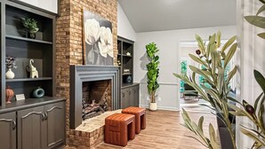 Ein Wohnzimmer mit Kamin, Holzboden, einer Ziegelwand und einer großen Pflanze.