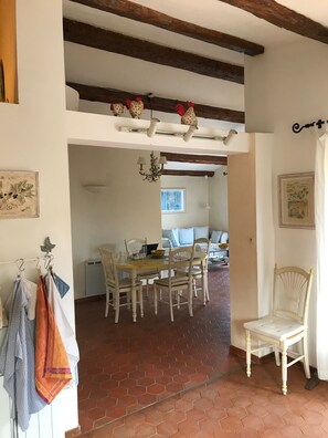 Ein Essbereich mit Backsteinboden, weißen Wänden und einer Holzzahlendecke. Es gibt zwei weiße Stühle, einen Tisch mit einem Laptop und eine Pendelleuchte.